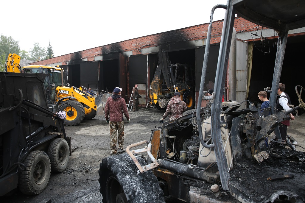 Работники пострадавших предприятий вытаскивают из гаража сгоревший экскаватор.